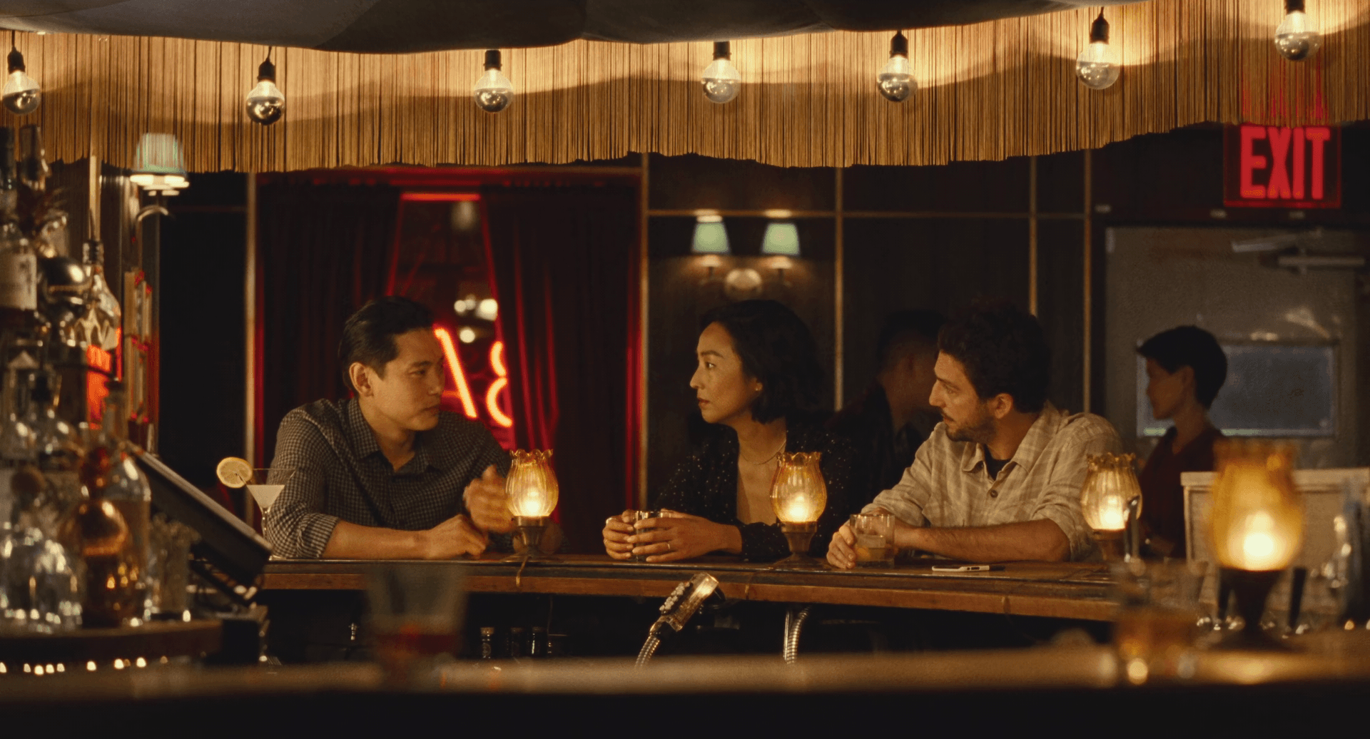 Past Lives opening scene, with the 3 characters sitting in a dimly lit bar